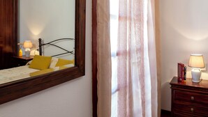 Un dormitorio con cama, lámparas de noche, mesita de noche, espejo y cortina.