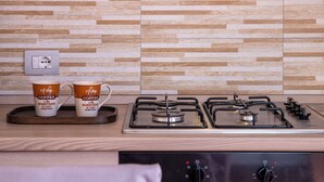 Una cocina con estufa moderna, dos tazas de café sobre una bandeja y una pared con diseño de baldosas geométricas.