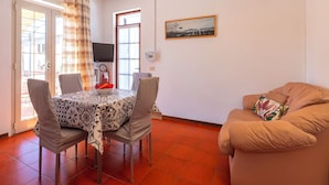 Un comedor con una mesa dispuesta para dos personas, un sofá y una televisión en la pared.