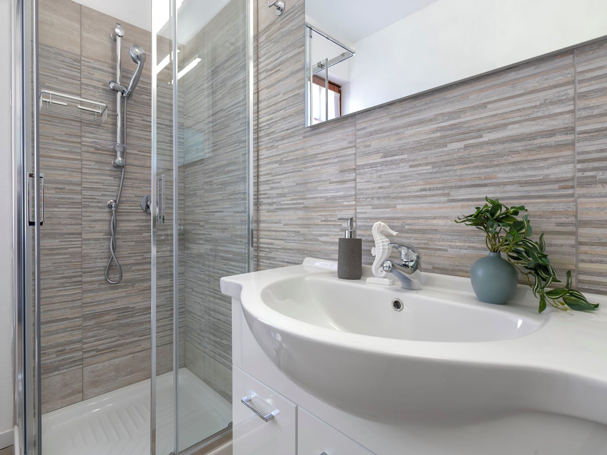 Ein modernes Badezimmer mit Duschkabine aus Glas, einem weißen Waschbecken mit dekorativer Armatur und einem Topf mit Pflanze.