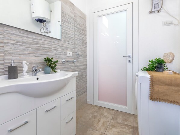 A modern bathroom with a white sink, a mirror, a towel rack, and a shower area.