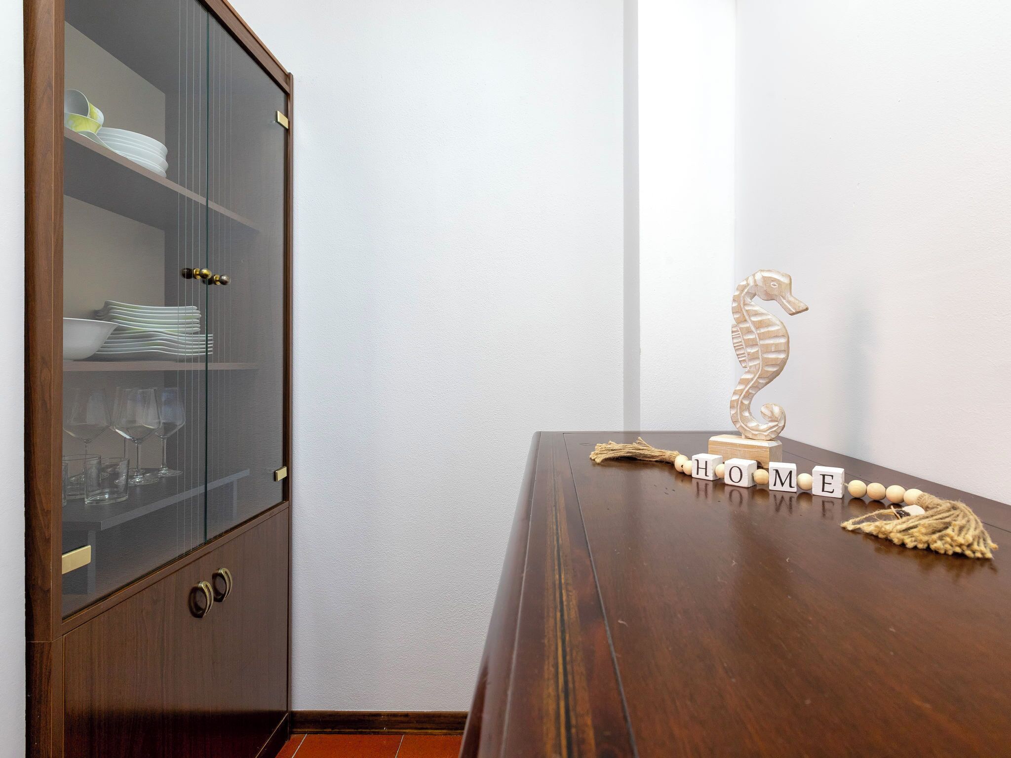 Un aparador de madera con puertas de cristal que contiene platos y vasos.