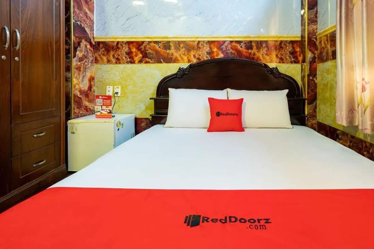 Une chambre d’hôtel comprenant un lit, une table de chevet, un petit réfrigérateur et un mur dont le motif ressemble à du marbre.