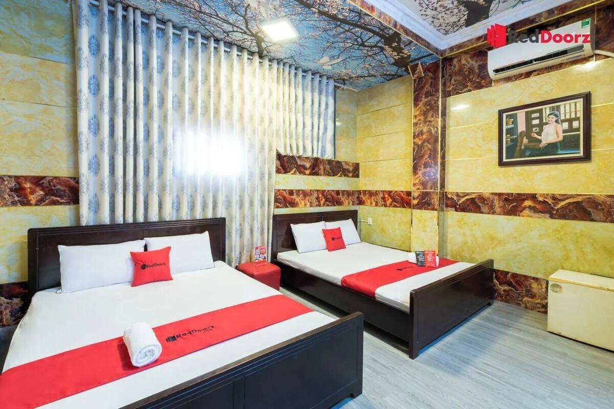 Une chambre d’hôtel avec deux lits, une couvre-lit rouge et blanche, un oreiller rouge et un tableau encadré au mur.