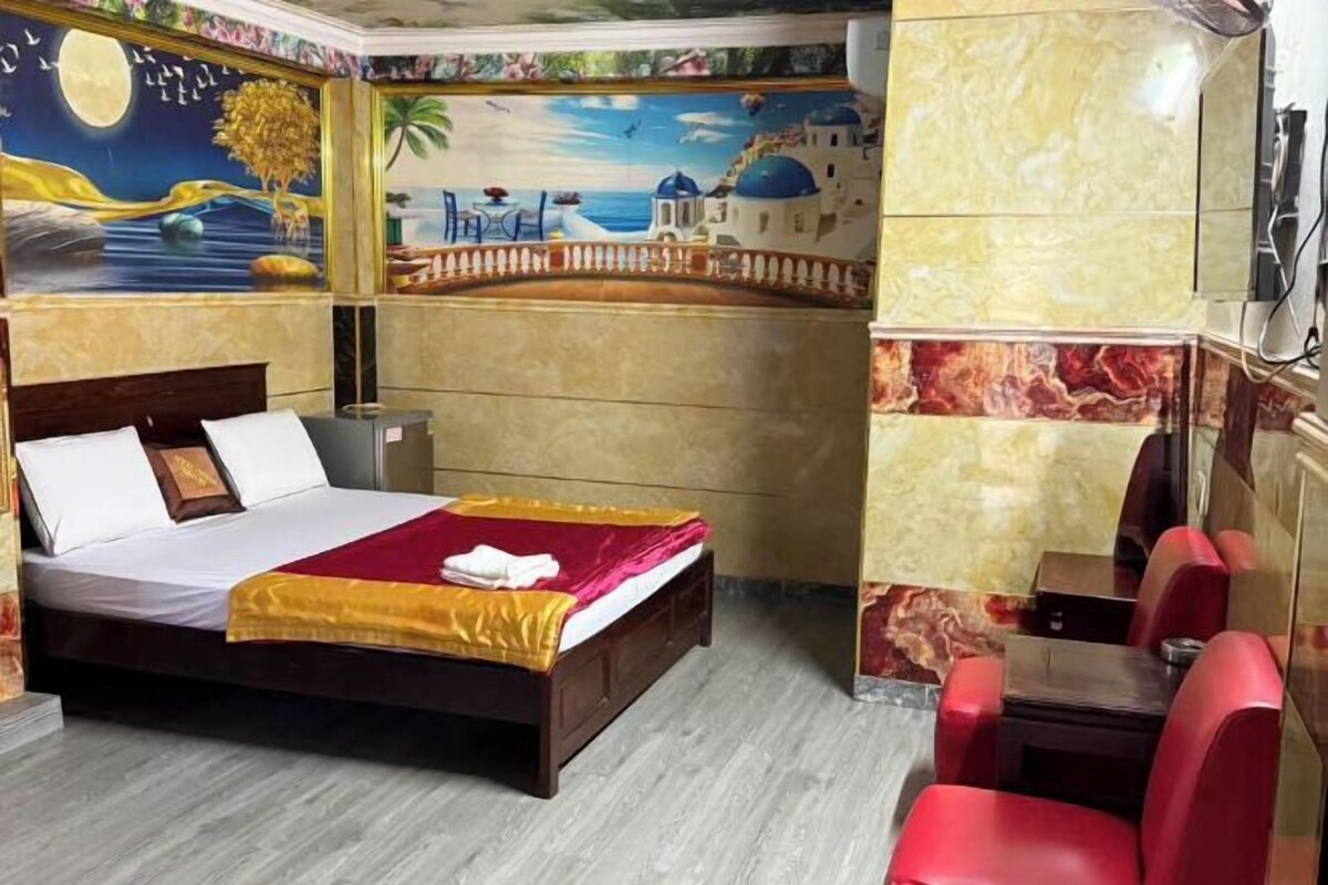 A hotel room with a bed, a desk, and a chair. The room has a mural on the wall depicting a beach scene.