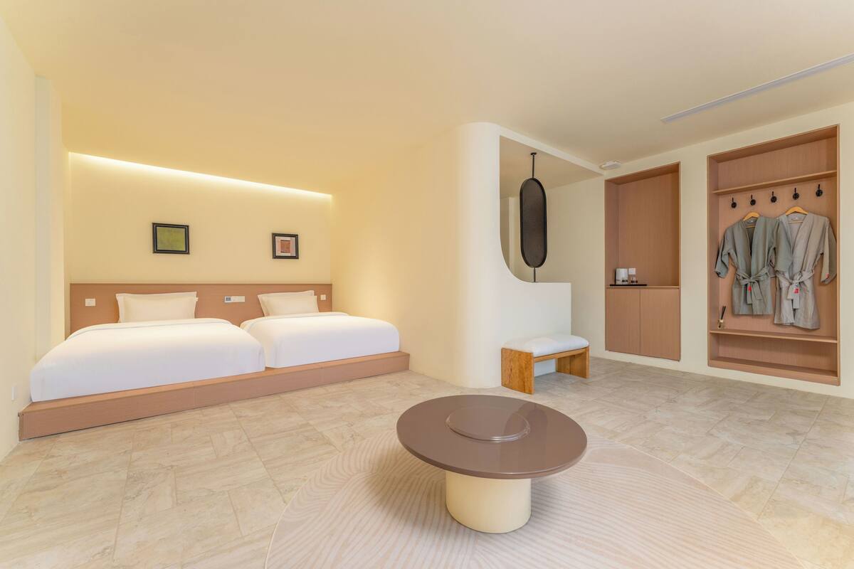 Una habitación de hotel moderna con una cama grande, una mesita pequeña y un vestidor con ropa colgada.