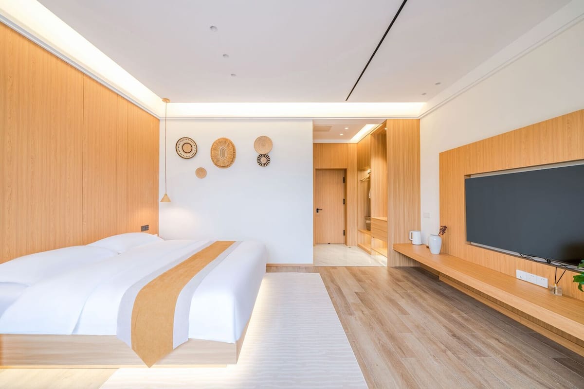 Una habitación de hotel moderna con una cama grande, paneles de madera, un televisor de pantalla plana y un vestidor.