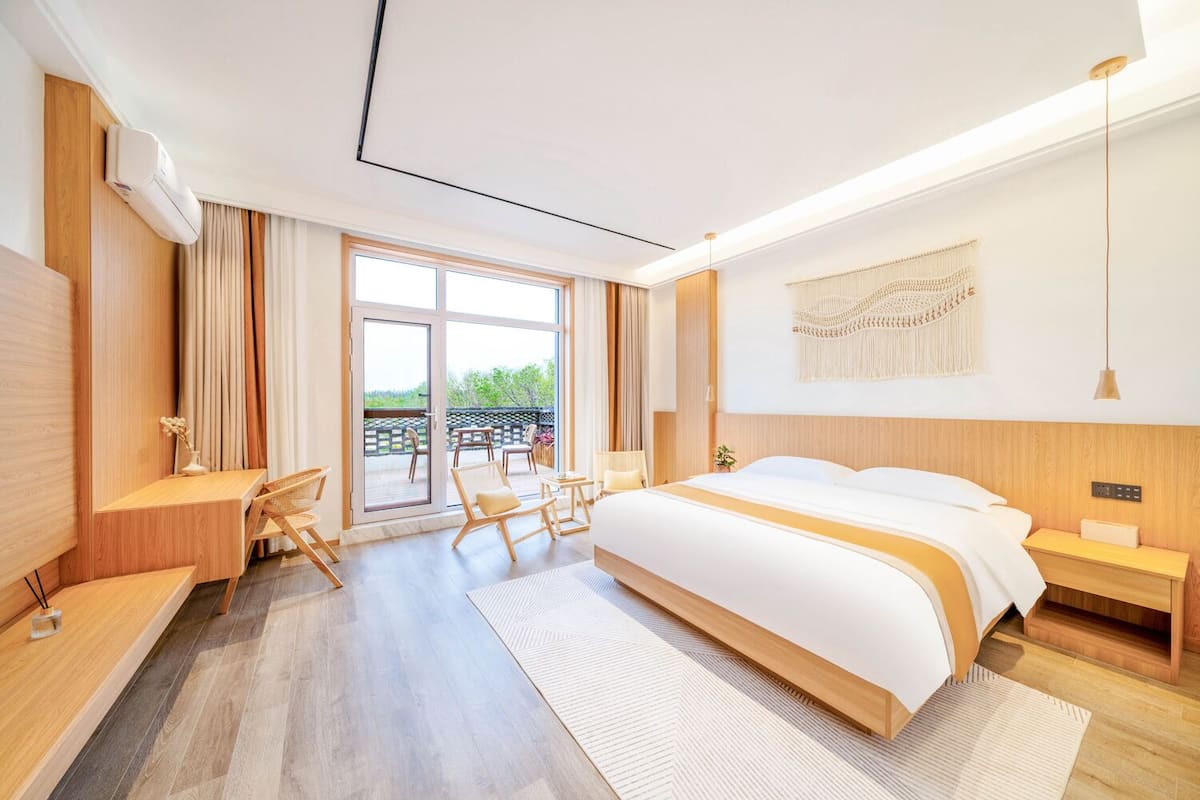 Una habitación de hotel moderna con una cama grande, un escritorio y un balcón con mobiliario exterior.