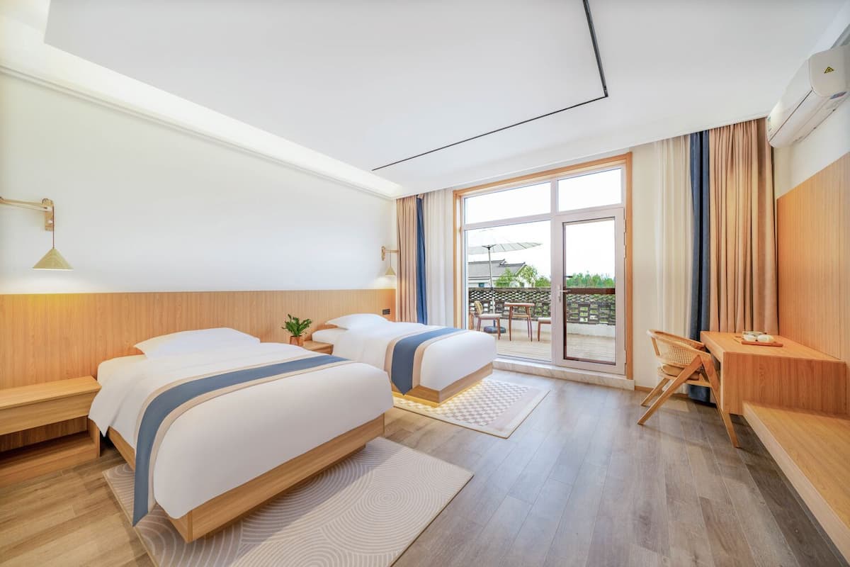 Habitación de hotel con dos camas, un escritorio y un balcón con mobiliario de exterior.
