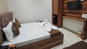 A modern bedroom with a bed, a wooden headboard, a TV mounted on the wall, and a ceiling fan. - Hotel RS INN (Amritsar)