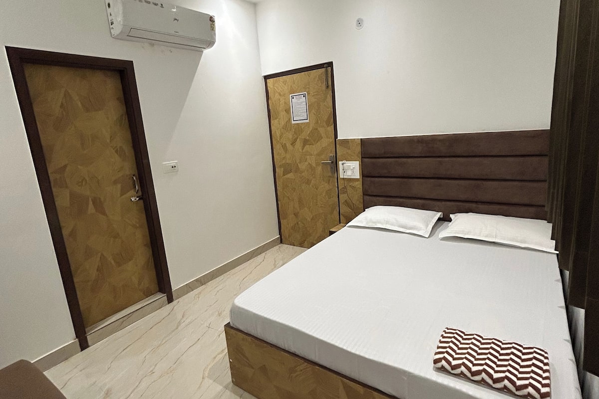Habitación de hotel con una cama, cabecero de madera, puerta de madera y unidad de aire acondicionado blanca en la pared.