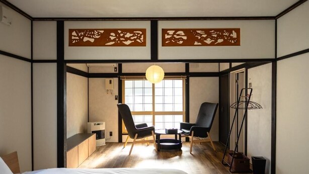 Ein traditioneller japanischer Raum mit Tatami-Boden, einem niedrigen Tisch, zwei Stühlen, einem Bett und einem großen Fenster mit Blick.