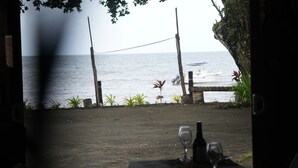 An outdoor dining area with a view of the sea, a table set with wine glasses and a bottle, and a rope barrier. - Natalei Eco Lodge  (Dawasamu)