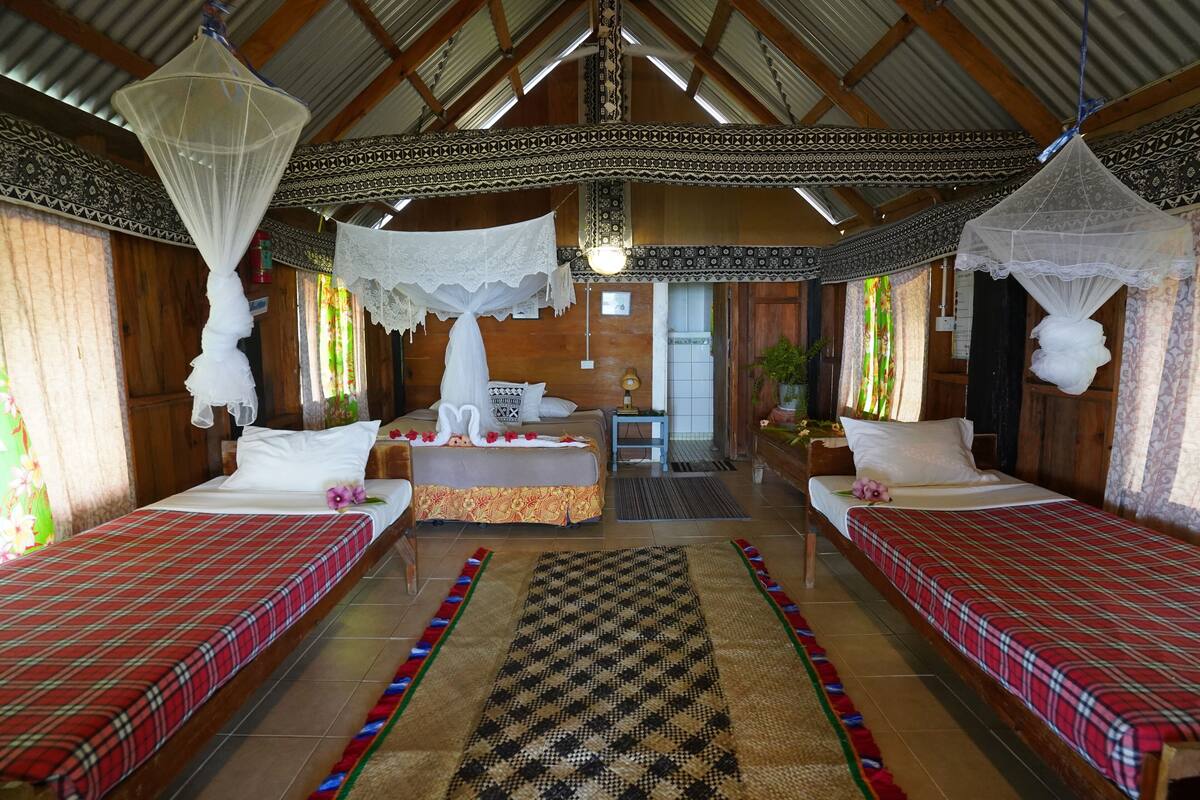Una habitación de madera tradicional con dos camas, cada una con una colcha escocesa roja, una cama central con un arreglo floral y una alfombra estampada.