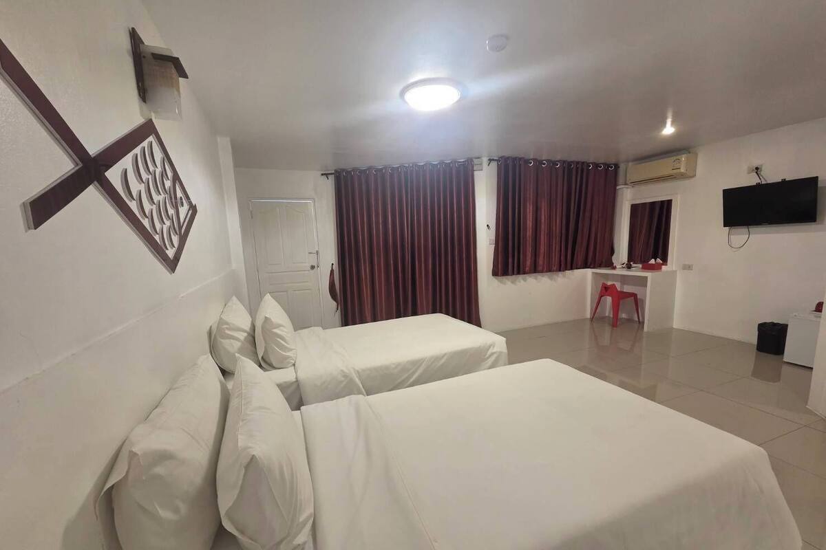 Ein Hotelzimmer mit zwei Betten, einem Schreibtisch, einem Stuhl, einem Fernseher und einer Klimaanlage.
