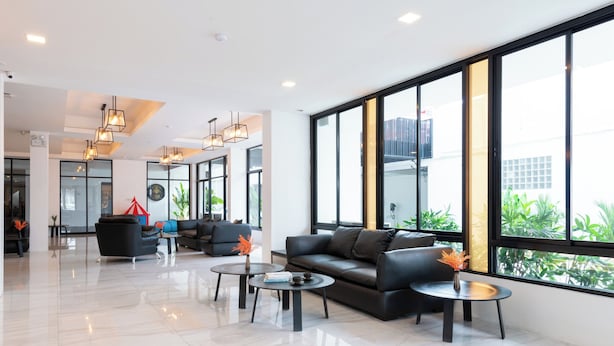 A modern lobby with a black leather sofa, round coffee tables, and pendant lighting. Large windows offer views of greenery outside. - Arawana Express North Pattaya (Pattaya)