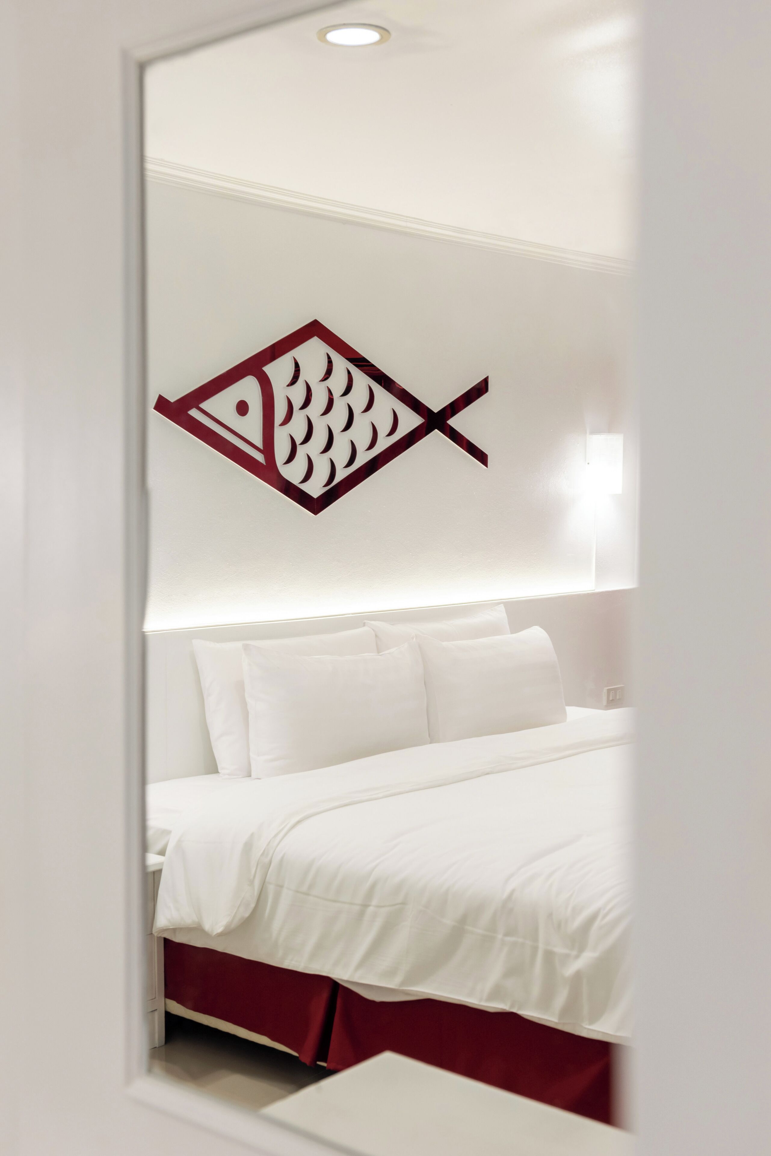 A hotel room with a bed, white bedding, and a wall-mounted fish decoration.