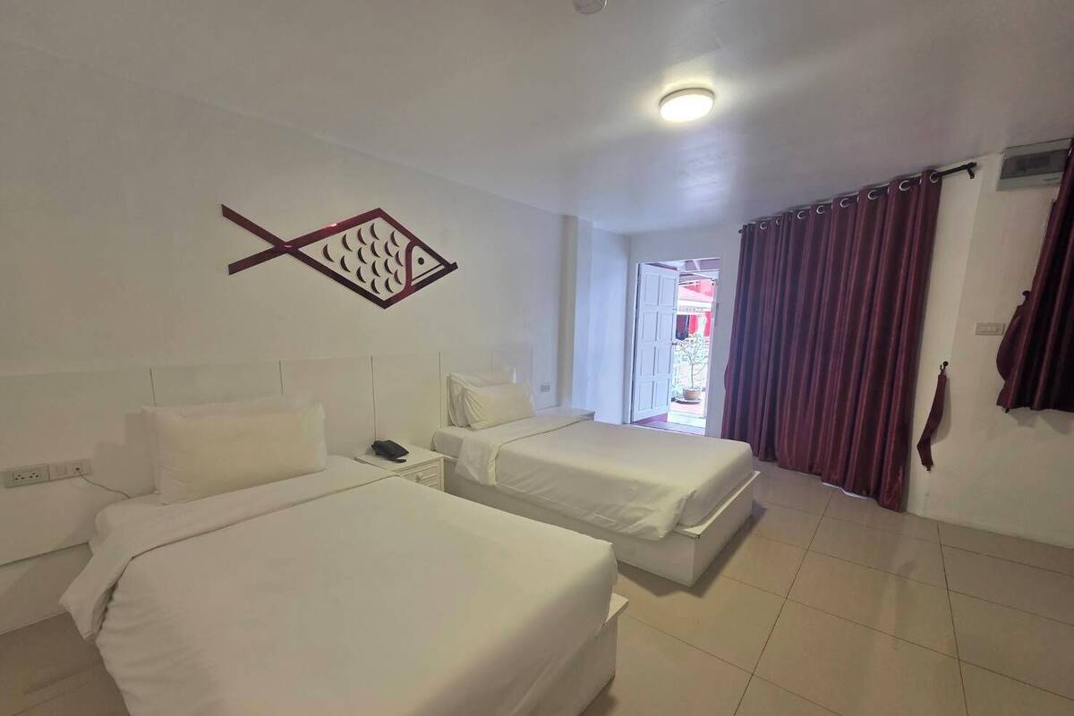 Ein Hotelzimmer mit zwei Betten, einem Wandbild von einem Fisch, einer Deckenleuchte und Blick nach draußen durch eine Tür.