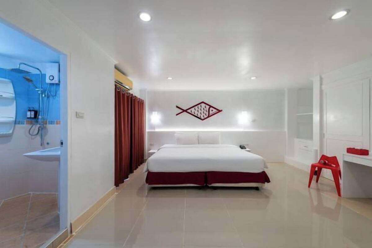 Ein modernes Hotelzimmer mit einem Bett, einem Schreibtisch, einem roten Sessel, einer Duschkabine und einer Wanddekoration mit einem Fisch.