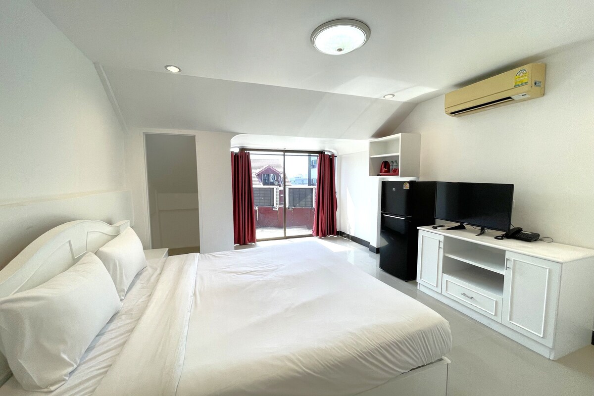 Habitación de hotel con cama, televisión, refrigerador y ventana con cortinas.