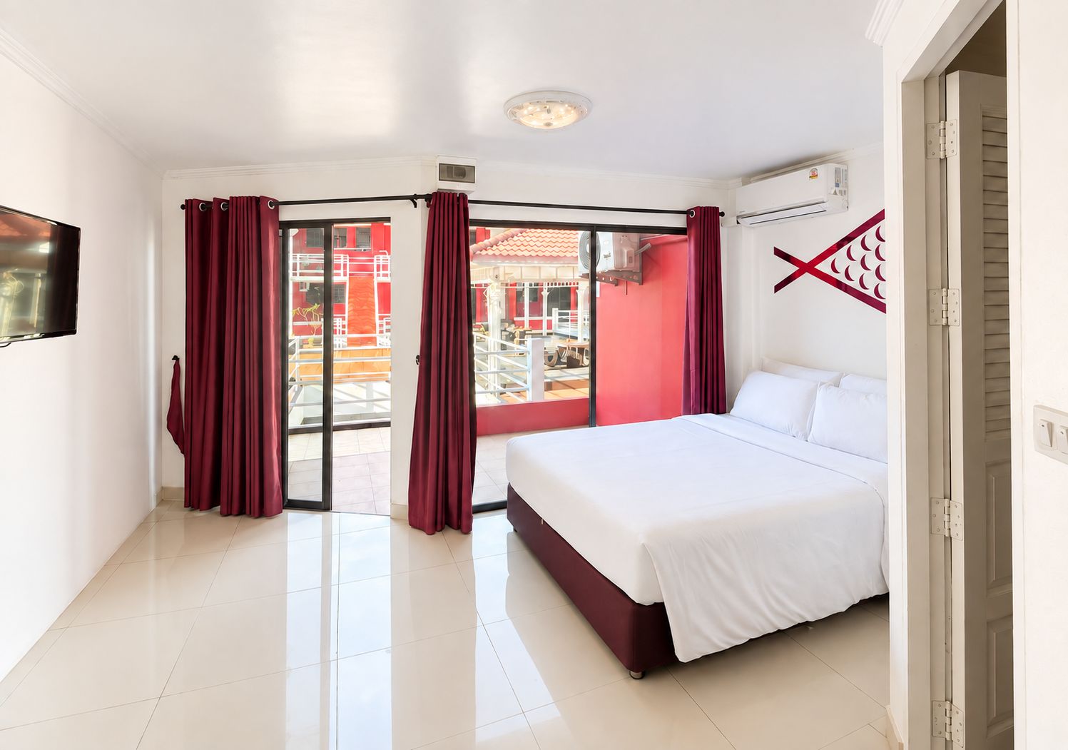 Quarto de hotel com uma cama, televisão e porta de vidro que se abre para o exterior.
