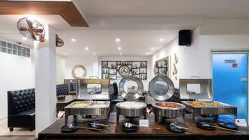 A buffet setup with various food containers, a seating area with leather chairs, and a wall with framed items.