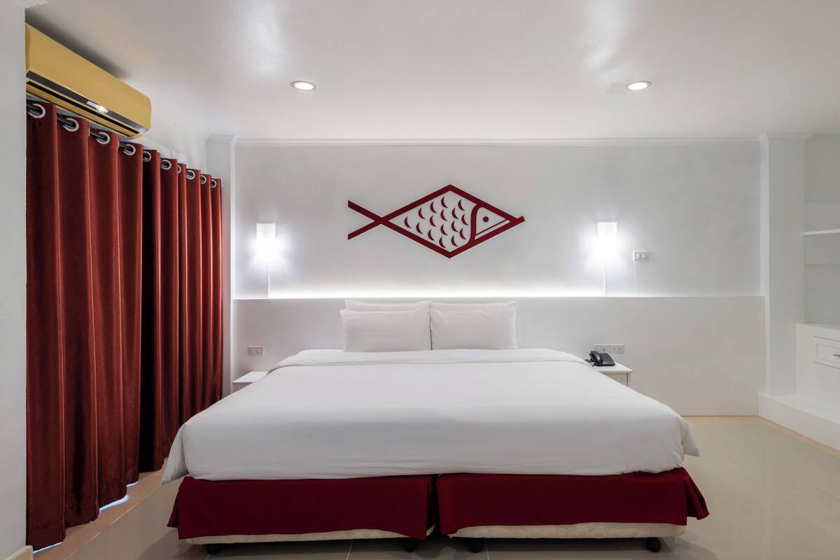 Ein modernes Hotelzimmer mit einem großen Bett, roten Vorhängen, einer Wanddekoration mit einem Fisch und einem Nachttisch mit Telefon.