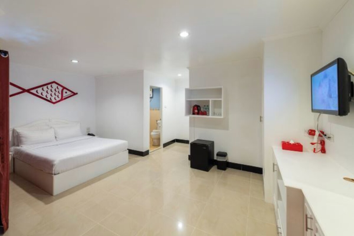 A modern hotel room with a bed, a TV, a small desk, and a wall-mounted shelf.