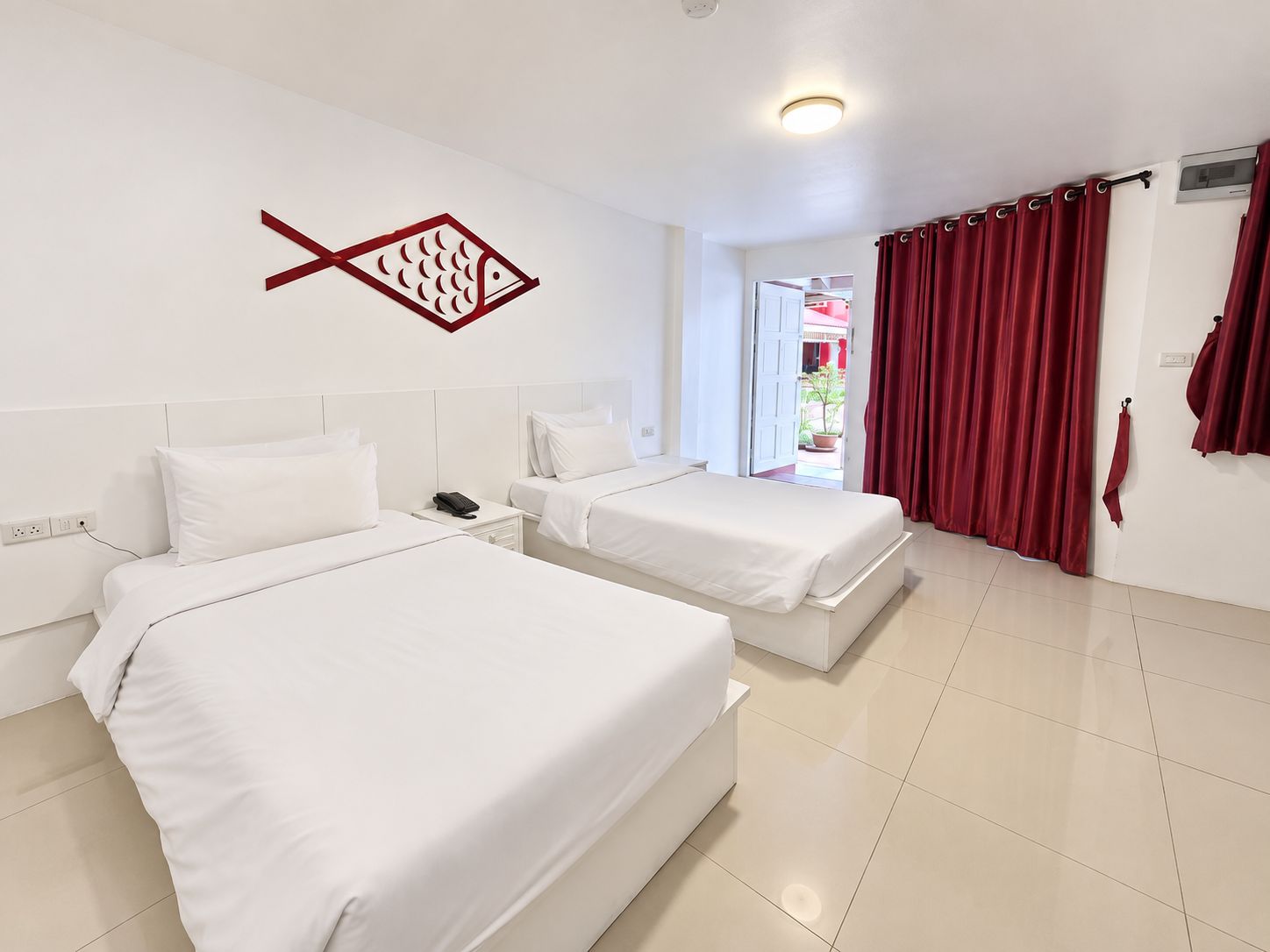 A hotel room with two beds, a red curtain, and a fish-shaped decoration on the wall.