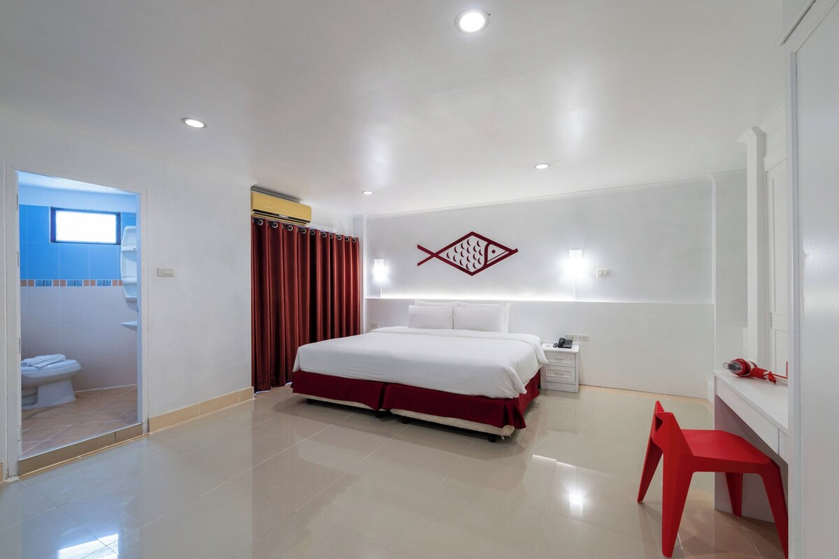 A modern hotel room with a large bed, a desk, and a red chair.