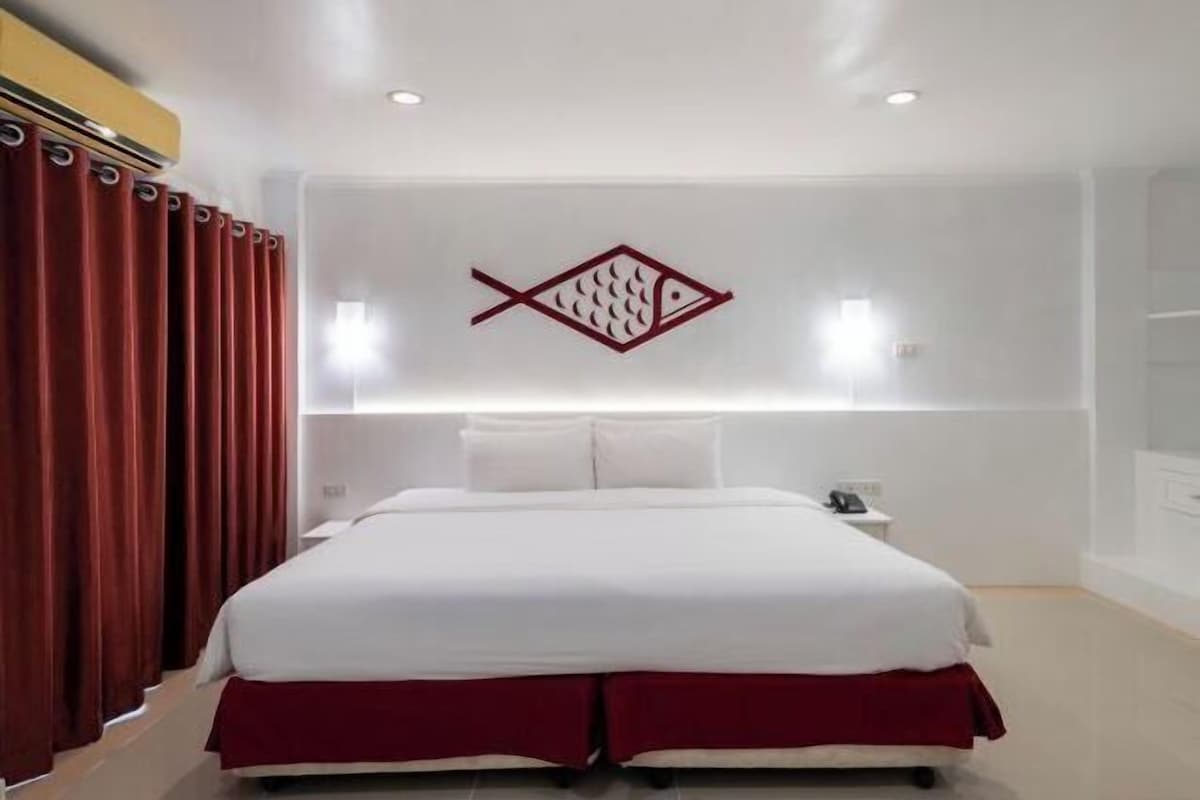 Une chambre d’hôtel avec un lit, des rideaux rouges, un symbole de poisson accroché au mur et une table de chevet.