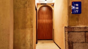 A hallway with a wooden door and a blue sign indicating an elevator. - Yuanjili International Youth Hostel (Qingdao)