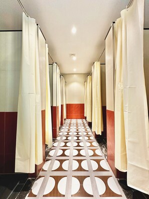 A hallway with multiple shower stalls, each with a curtain. The floor has a geometric pattern. - Yuanjili International Youth Hostel (Qingdao)