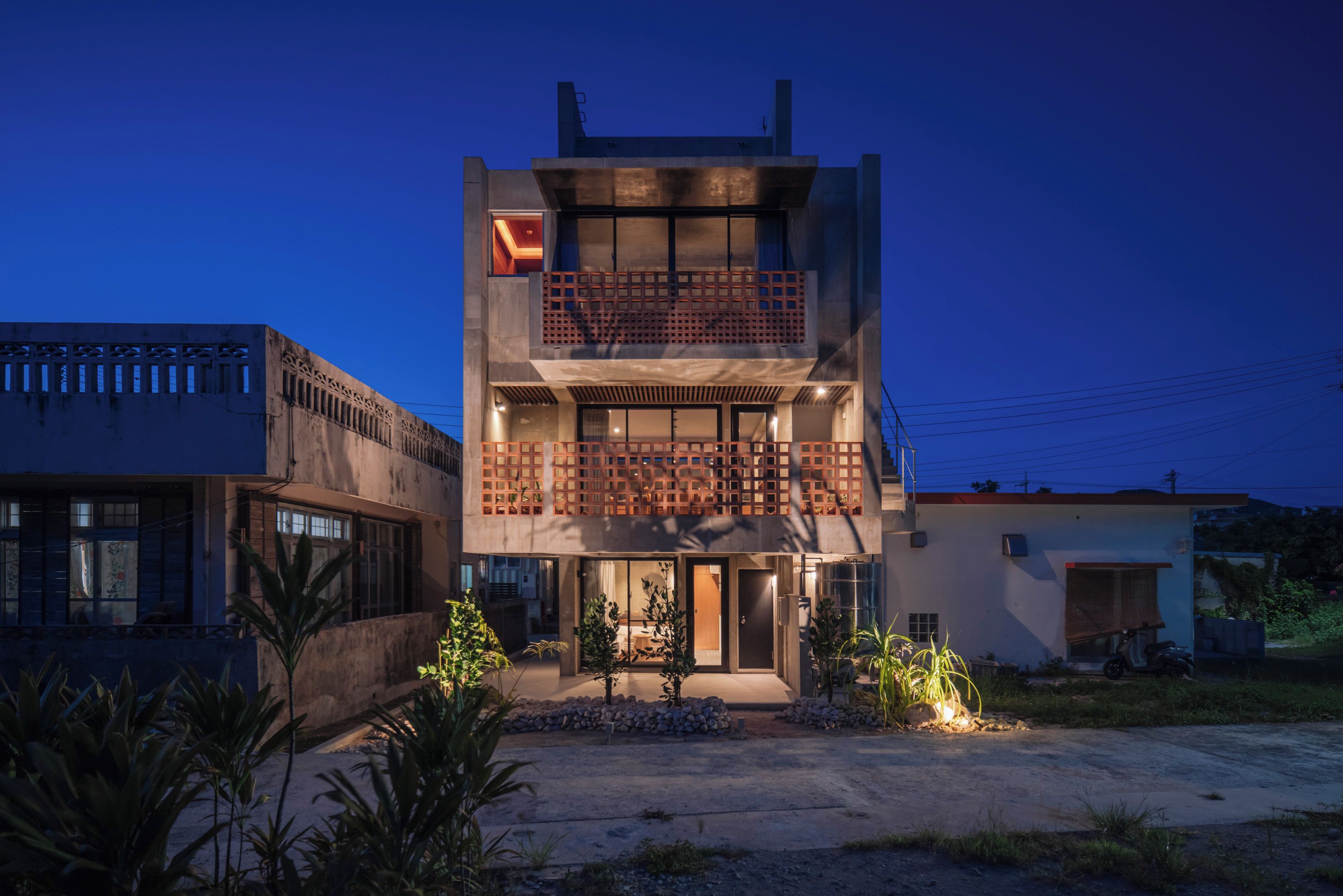 Un immeuble à plusieurs étages doté d’un balcon à l’étage supérieur, d’une entrée de garage et d’une allée menant à la porte d’entrée.