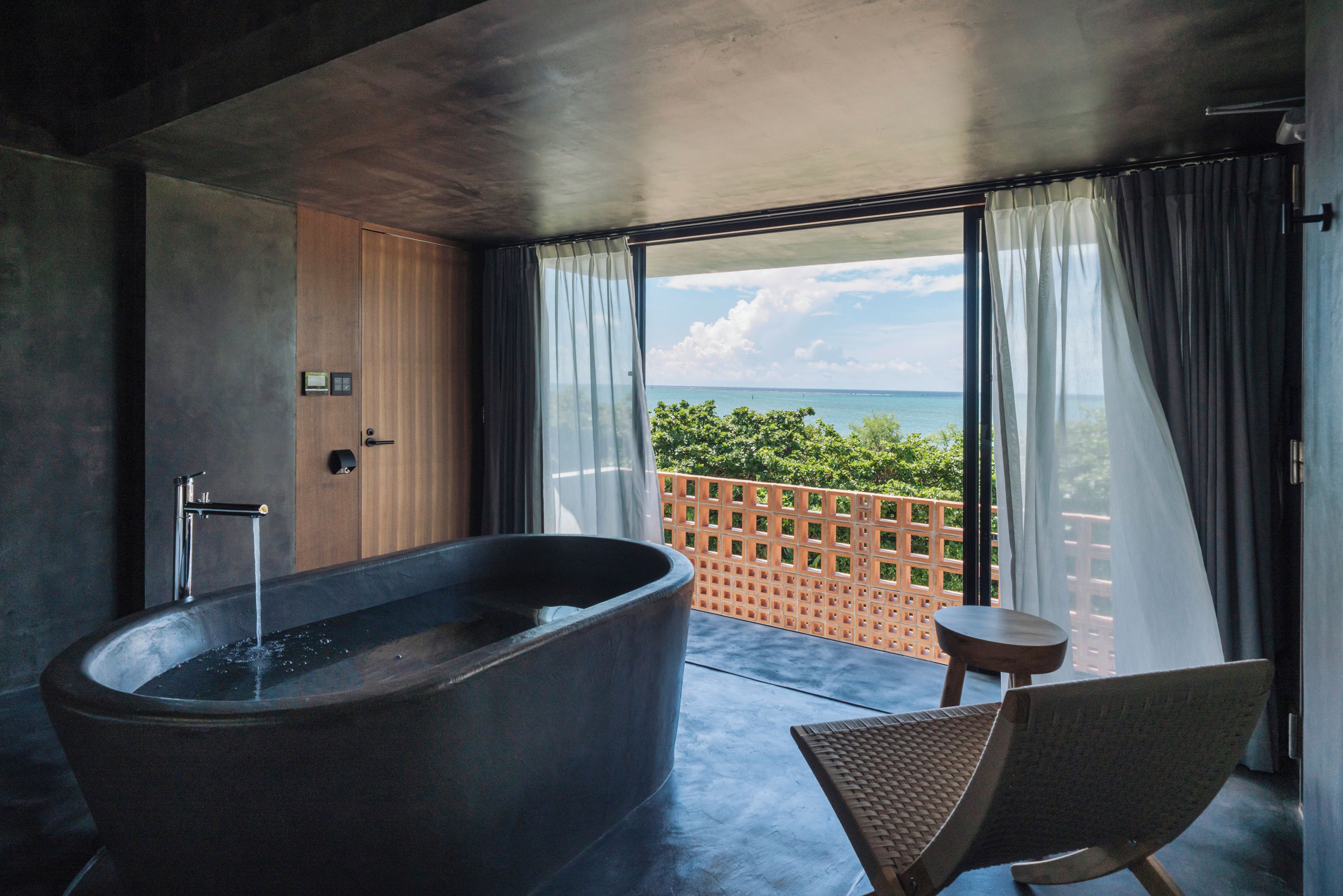 Une salle de bain moderne avec une baignoire sur pieds, une petite table ronde et une vue sur la mer grâce à de grandes fenêtres.
