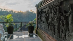A balcony with potted plants and a detailed stone carving. - Grand Campuhan (Sebatu)