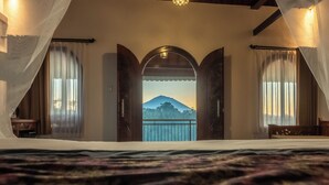 A bedroom with a large bed, a view of a mountain through an arched doorway, and curtains on the windows. - Grand Campuhan (Sebatu)