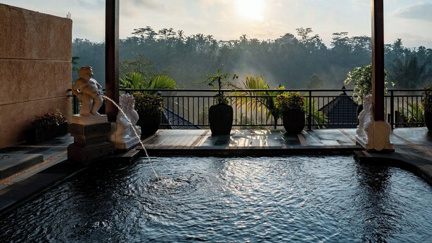 A serene outdoor water feature with statues, surrounded by potted plants and a view of a forested landscape. - Grand Campuhan (Sebatu)