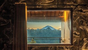 A room with a large window, a curtain, and a view of a mountain. - Grand Campuhan (Sebatu)