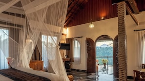 A room with a bed, a nightstand, a lamp, a wooden cabinet, and a balcony with a view of the mountains. - Grand Campuhan (Sebatu)