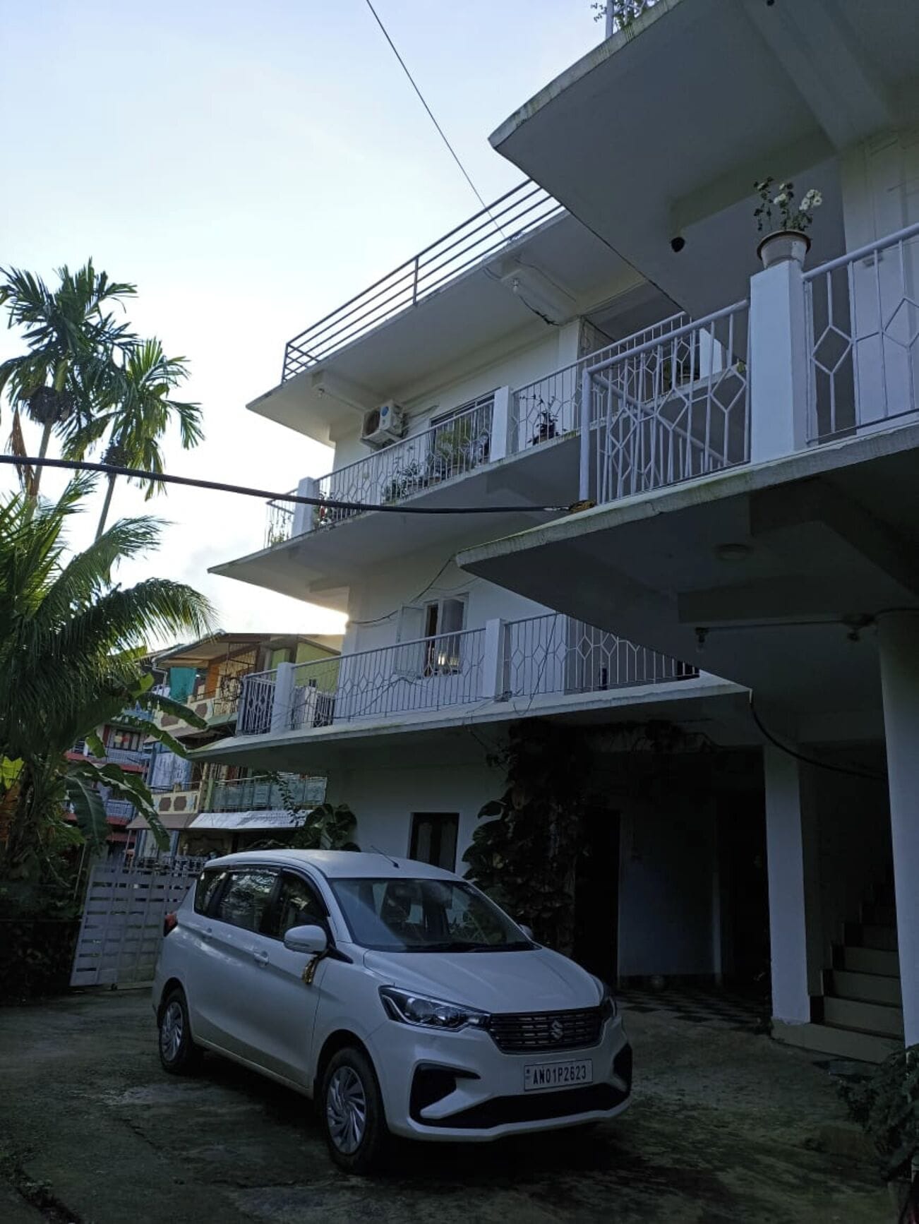 A multi-story residential building with balconies, a parked car, and a staircase leading to the entrance.