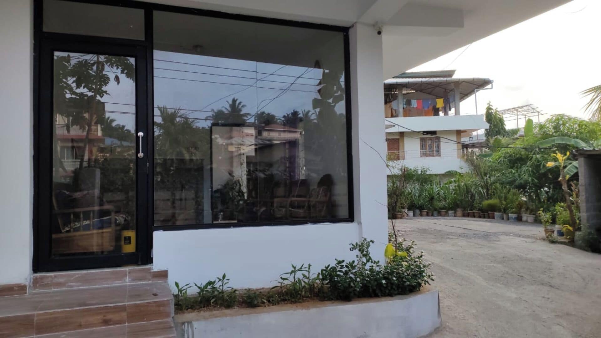 A modern building with a large glass door and windows, a concrete pathway, and a small garden area.