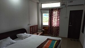 A hotel room with a bed, a chair, a window with curtains, and an air conditioning unit.