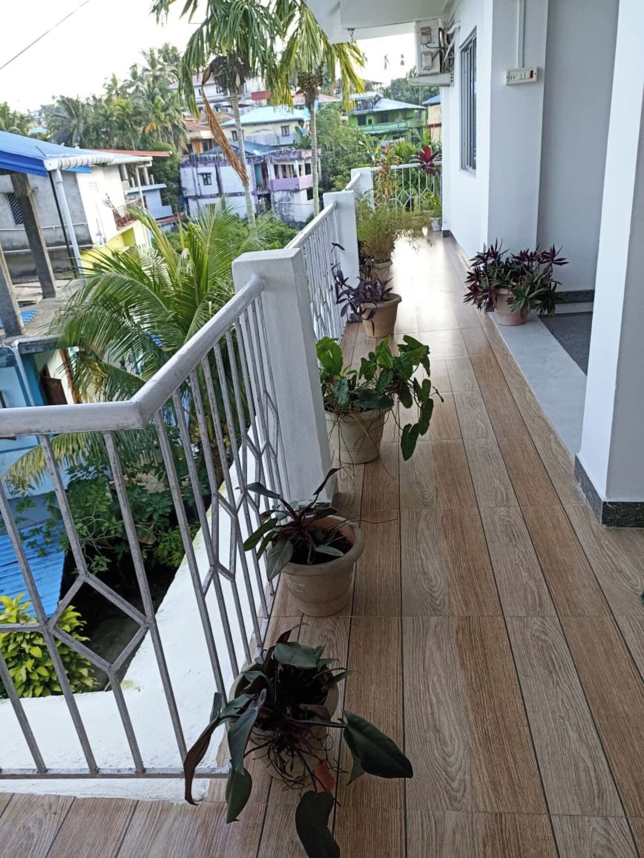 A balcony with a railing, potted plants, and a view of neighboring buildings.