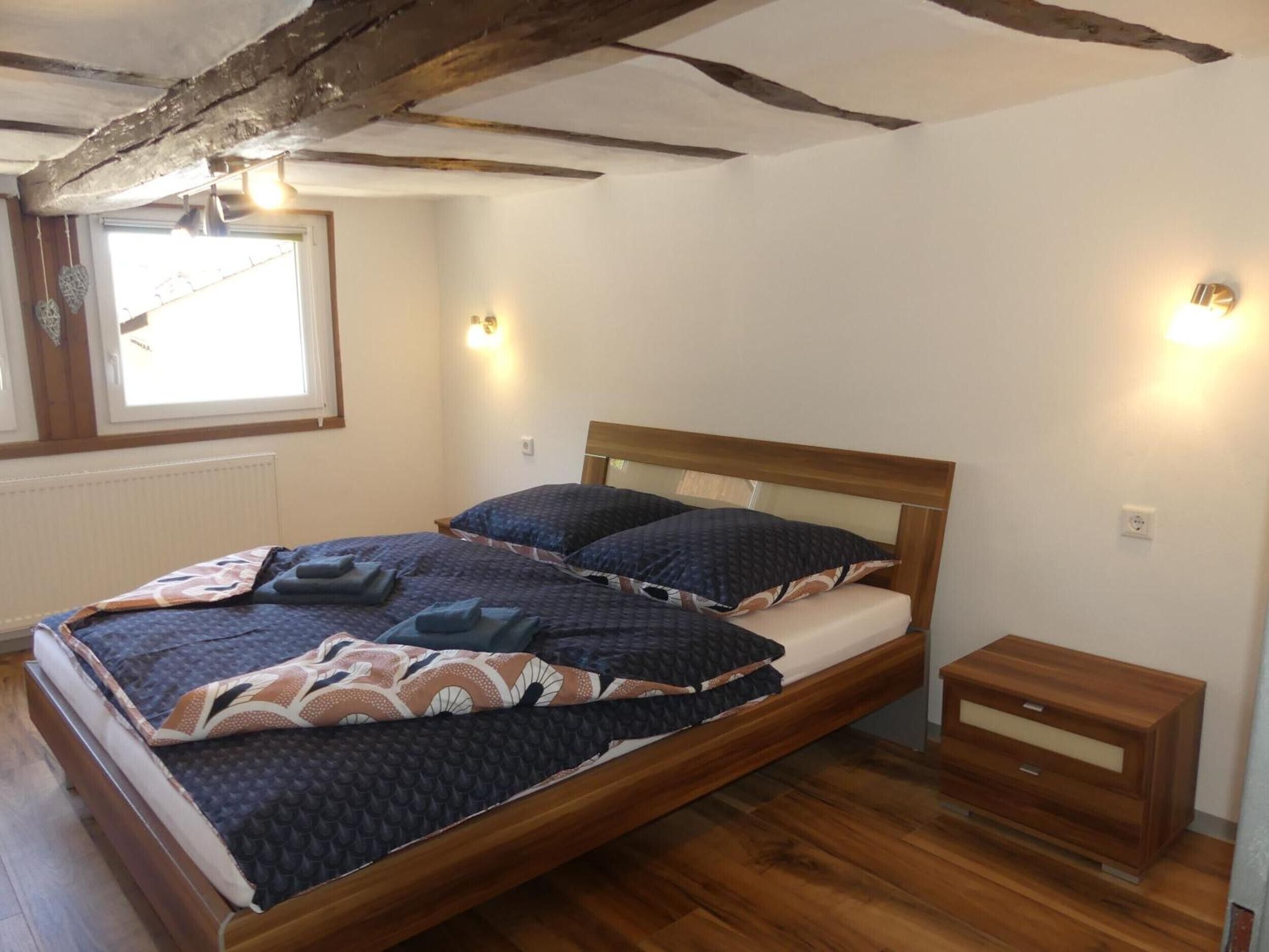 Un dormitorio con cama de madera, mesitas de noche y ventana con persianas.