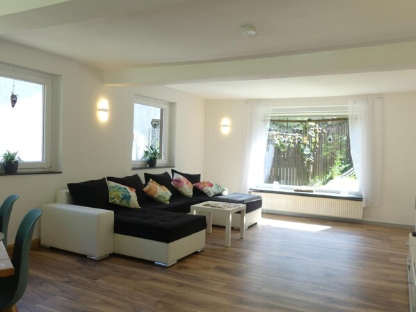 A modern living room with a sofa, a coffee table, and a dining area. - Holiday Home Villa Wolffsschlucht (Oberzent)