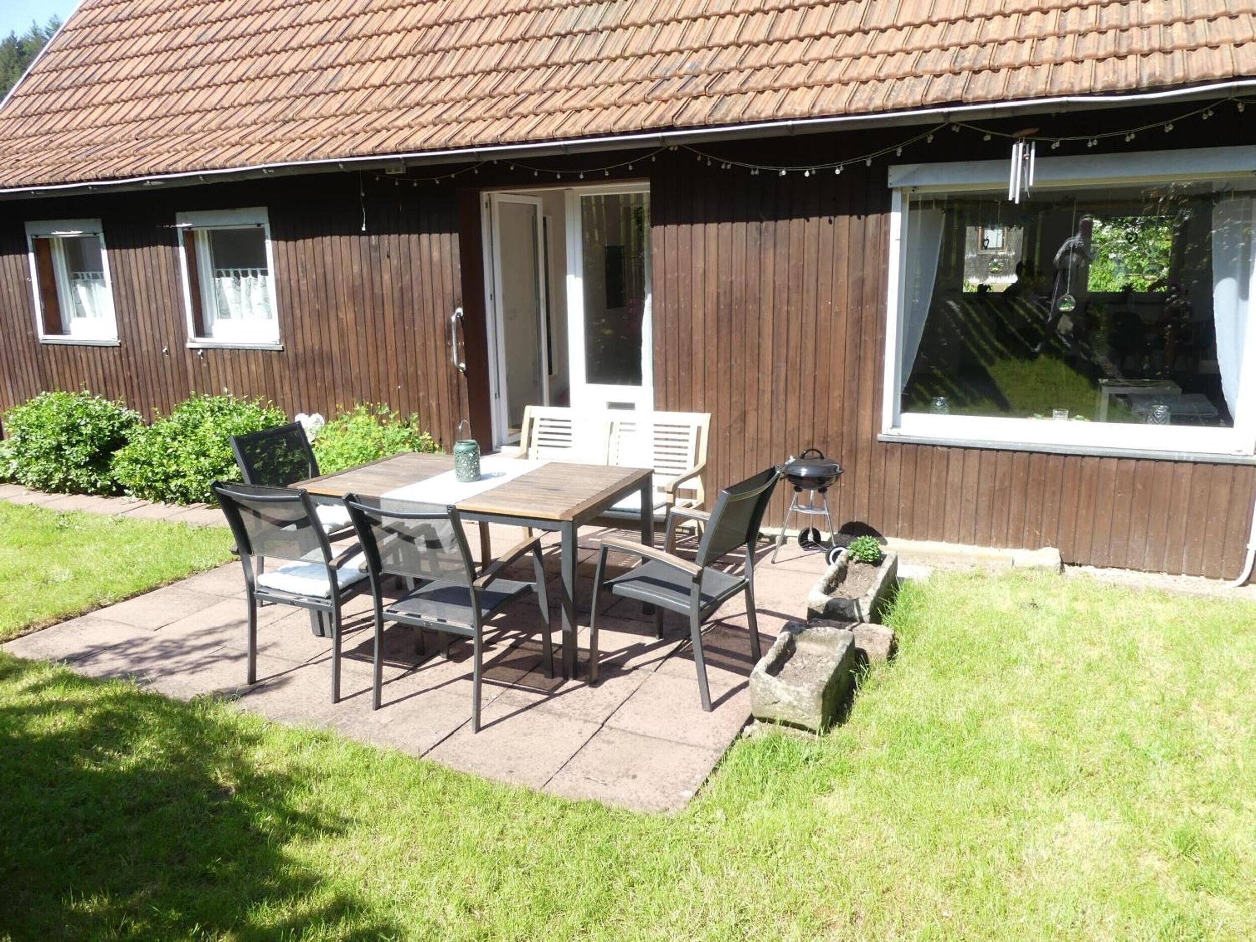 A house with a patio, a table with chairs, a barbecue grill, and a window.