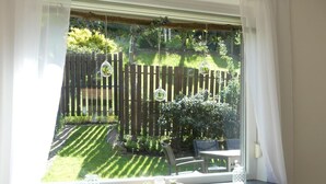 Ein Zimmer mit Fensterblick auf einen Garten, einem Heizkörper und einem Tisch mit Vase und Pflanze.