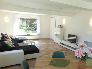 A modern living room with a sofa, TV, and a dining table with chairs. - Holiday Home Villa Wolffsschlucht (Oberzent)