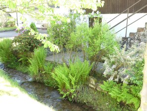 A garden with a stream, various plants, and a building in the background. - Holiday Home Villa Wolffsschlucht (Oberzent)